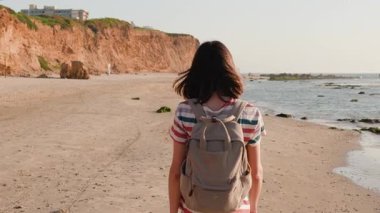 Sırt çantalı bir kadın gezgin kumlu deniz kıyısı ya da okyanus kıyısında yürüyor. Doğaya yaz gezisi. Yürüyüş ve seyahat.