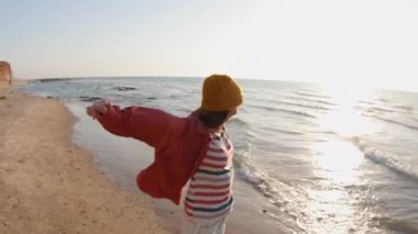 Mutlu neşeli kız sahilde eğleniyor. Sahilde kollarını sallayarak koşan çekici bir kadın. Gülümseyen neşeli bayan sahilde eğleniyor ve güzel doğanın tadını çıkarıyor..