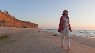 Pozitif kız sahilde yürümekten hoşlanır. Genç kız sahilde yürüyor. Kumsalda tişörtlü ve şapkalı bir kız. pozitif ruh hali.