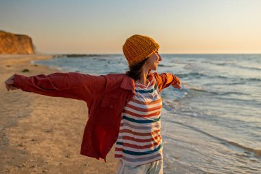 Gülümseyen neşeli kız sahilde eğleniyor anın tadını çıkarıyor. Plajda yürüyen tişörtlü bir kadın. Tatilde bir turist. Seyahat ve macera.