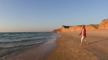 Pozitif kız sahilde yürümekten hoşlanır. Genç kız sahilde yürüyor. Kumsalda tişörtlü ve şapkalı bir kız. pozitif ruh hali.