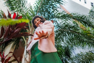 Moda kıyafetleri içinde gülümseyen genç, güzel bir hippi kadın. Geniş gülümseyen bir kızın portresi. Kız pembe gömlek ve yeşil pantolon giyiyor. şehir giyim tarzı. 