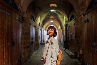 Kameralı kız. Sırt çantası ve kamerası olan şık bir kız eski şehrin caddesinde duruyor. Maceralar ve seyahat.