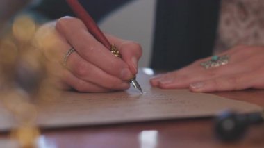 Masada oturan ve mürekkep ve kalemle yazan bir kız. Kaligrafi, güzel mektup. Yakın plan..