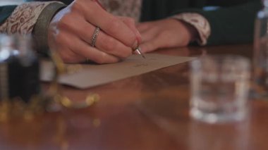 Masada oturan ve mürekkep ve kalemle yazan bir kız. Kaligrafi, güzel mektup. Yakın plan..