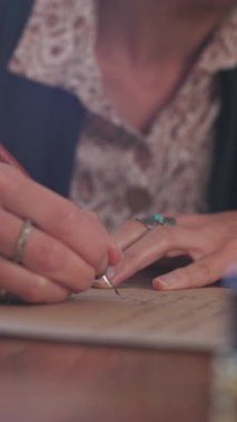 Dikey çekim. Masada oturan ve mürekkep ve kalemle yazan bir kız. Kaligrafi, güzel mektup. Yakın plan..
