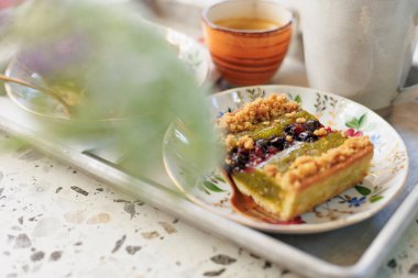 Açık bir kafede, üzerinde fıstık ve kahve olan bir parça fındıklı kek.