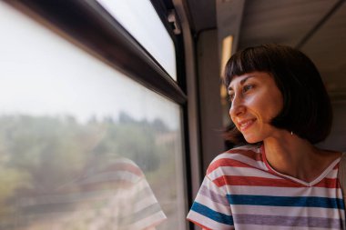  Genç ve güzel bir kadın tren yolculuğundan zevk alıyor, pencerenin yanında oturuyor ve pencereden dışarı bakıyor. Tren yolculuğu. İyi yolculuklar. tren yolcu.