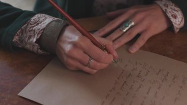 Kız kalemi mürekkebe batırıyor. Kız masaya oturur ve kalem ve mürekkeple yazar. Kaligrafi, güzel mektup. Yakın plan..