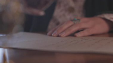 Kız kalemi mürekkebe batırıyor. Kız masaya oturur ve kalem ve mürekkeple yazar. Kaligrafi, güzel mektup. Yakın plan..
