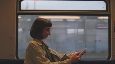 Trende gülümseyen güzel bir kızın portresi. Akıllı telefon kullanıyor, arkadaşlarıyla sohbet ediyor, el ele tutuşan bir kadın. Trenle seyahat eden bir kız..