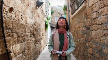 Gülümseyen, kameralı güzel bir bayan turist şehrin eski turistik bölgesinde boş caddede yürüyor ve tatilin tadını çıkarıyor. Popüler turistik yerleri gezmek.