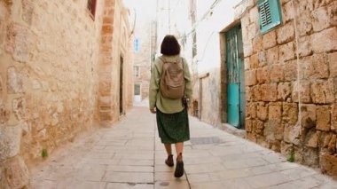 Yolculuk sırasında eski şehrin caddesinde gezen sırt çantalı çekici genç turist mimariye hayran kalıyor, etrafa bakıyor. İsrail 'in Akko kenti
