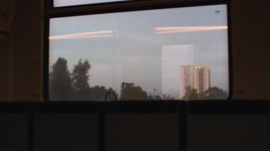 Tren vagonundan manzara. Şehir manzarası pencereden görülebilir. Gökdelenler gökyüzüne yükselir, cam batan güneşin altın ışığını yansıtır. İsrail.