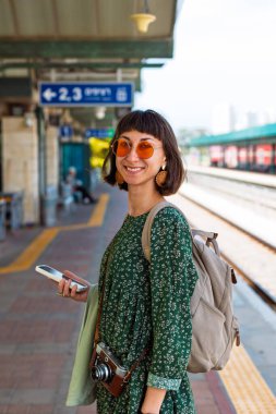 İstasyonun platformunda kamera ve sırt çantasıyla bekleyen genç ve güzel bir kız başvuru formundaki tren saatlerine bakıyor. İyi yolculuklar..