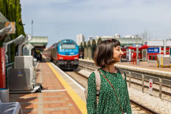 Kız saate bakıyor ve treni bekliyor. Tren istasyonunda tren bekleyen bir kız. özgürlük ve seyahat kavramı.