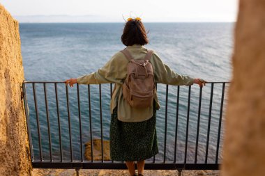 Turist denize bakıyor. Sırt çantalı kız sakin deniz manzarasının tadını çıkarıyor. Kız seyahat eder.