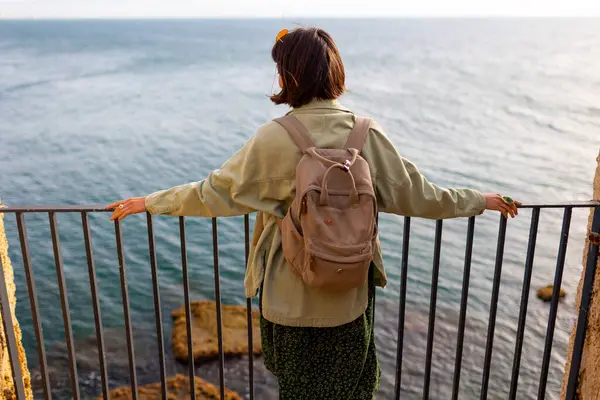 Sırt çantalı kız sakin deniz manzarasının tadını çıkarıyor. Kız seyahat ediyor. Turistler denize bakar..