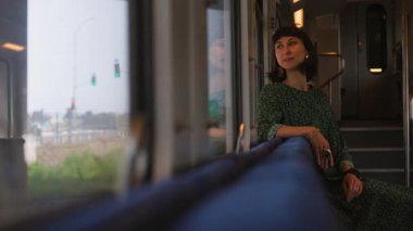 Trendeki kadın pencerenin yanında oturur ve pencereden dışarı bakar. Bir kadın gezgin trenin camından dışarı bakar ve sürmekten zevk alır. bir tren yolcusu.