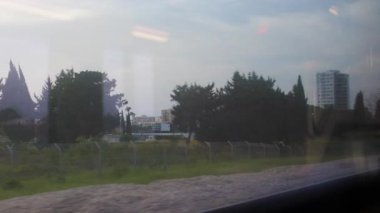 Tren vagonundan manzara. Şehir manzarası pencereden görülebilir. Gökdelenler gökyüzüne yükselir, cam batan güneşin altın ışığını yansıtır. İsrail.