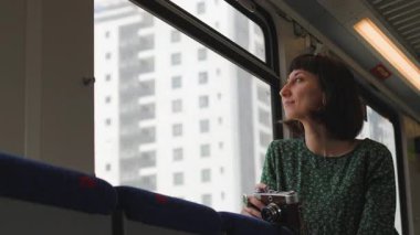 Elinde kamera olan genç bir kız tren penceresinden şehre bakıyor. Tren yolculuğu. Tren yolcusu. Kameralı kız.
