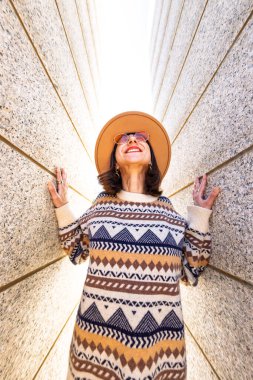 Moda kıyafetleri içinde gülümseyen genç ve güzel bir hippi kadın. Açık havada pozitif model. Güneş gözlüğü ve şapkayla neşeli ve mutlu.