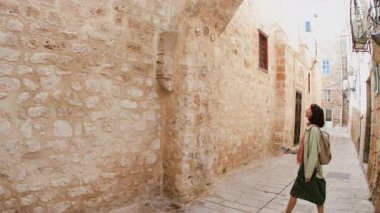 Kız turist eski şehrin caddesinde yürüyor ve telefonla manzaranın fotoğrafını çekiyor. Şehirde telefonu olan bir kız. seyahat ve macera.