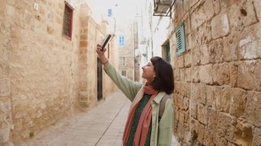 Kız turist eski şehrin caddesinde yürüyor ve telefonla manzaranın fotoğrafını çekiyor. Şehirde telefonu olan bir kız. seyahat ve macera.