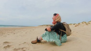 Kumda oturan ve denize bakan bir kız. Sırt çantalı genç bir kız seyahat ediyor..