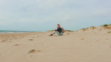 Kumda oturan ve denize bakan bir kız. Sırt çantalı genç bir kız seyahat ediyor..