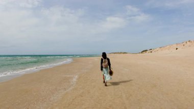 Seyahat ve tatil. Sırt çantalı şık bir kız rüzgarlı bir havada kumsalda yürüyor. Kız kumsalda yürüyor..
