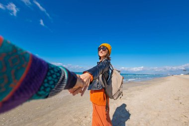 Sahilde erkek arkadaşıyla gezinin tadını çıkaran bir kadın, dikiz manzaralı. Seyahat eden çift. Kız ve erkek el ele tutuşuyor. Sahilde yürü..