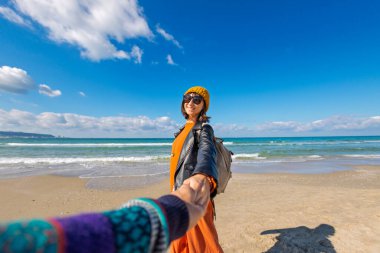 Sahilde erkek arkadaşıyla gezinin tadını çıkaran bir kadın, dikiz manzaralı. Seyahat eden çift. Kız ve erkek el ele tutuşuyor. Sahilde yürü..
