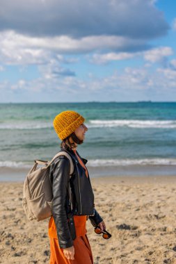 Sırt çantalı bir kız. Sırt çantalı şık bir kadın soğuk ve güneşli bir günde plaja gitmekten hoşlanır. Yaşam tarzı, seyahat, turizm, doğa, aktif yaşam.