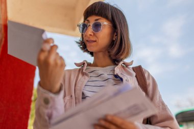 Posta kutusunun yanında duran zarfları karıştıran kadına yaklaş. Ödeme makbuzlu mektup.