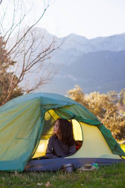 Mutlu, gülümseyen bir çocuk, dağların arka planında çadırda oturuyor. Çadırdaki çocuk. Açık hava eğlencesi. Çocuklarla kamp ve yürüyüş..