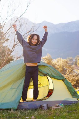 Mutlu çocuk çadırdan çıkar ve dağlara bakar. Çadırdaki çocuk. Açık hava eğlencesi. Çocuklarla kamp ve yürüyüş..