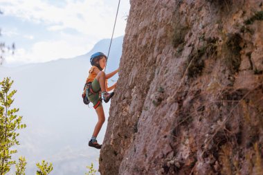 Dağcı çocuk. Çocuk kaya tırmanışı çalışıyor. Yaz kampı. Doğada spor. Sevimli bir genç kayaya tırmanıyor, spor insanları yaşam tarzı konseptiyle.
