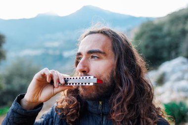 Müzisyen sokakta dururken mızıka çalmaktan hoşlanıyor. Uzun saçlı genç bir adam mızıka çalıyor..