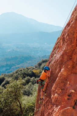 Çocuk yaz kampında kaya tırmanışı yapıyor. Dağcı çocuk. Doğada spor. Sevimli genç, kayaya bağlanmış bir şekilde tırmanıyor. Aktif tatil. Yaz tatili.