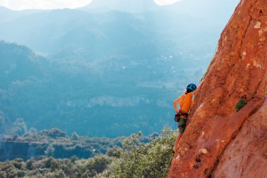 Çocuk yaz kampında kaya tırmanışı yapıyor. Dağcı çocuk. Doğada spor. Sevimli genç, kayaya bağlanmış bir şekilde tırmanıyor. Aktif tatil. Yaz tatili.