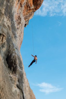 İple tırman. Genç bir adam kaya tırmanışı ile meşgul, yukarıdan bir atlet iniyor mavi gökyüzünün arka planında bir halat üzerinde.