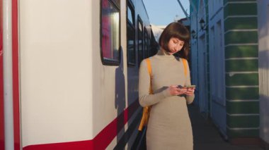 Umumi bir tren istasyonunda beklerken akıllı telefonunu kullanan bir bayan turist. Tren istasyonundaki bir mesaja cevap veren çekici bir genç kız..