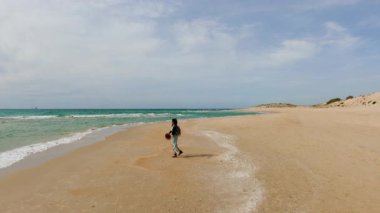 Seyahat ve tatil. Sırt çantalı şık bir kız rüzgarlı havada kumlu sahilde yürümekten hoşlanır. Kumsalda yürüyen kız.