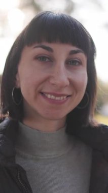 Dikey çekim. Parktaki kız. Mutlu kız gülümsüyor ve kameraya bakıyor. Genç kız doğada dinleniyor ve anın tadını çıkarıyor..