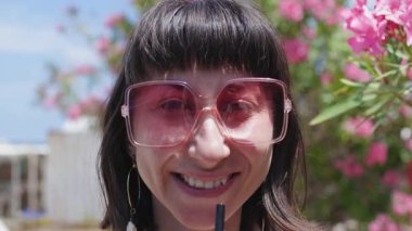 Kız plastik bardakta samanla kokteyl tutuyor ve içiyor. Şık güneş gözlüklü, sokakta poz veren güzel bir kız..