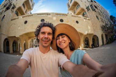 Yaz kıyafetleri içinde genç bir çift şehir caddesinde yürürken birbirlerine sarılıp selfie çekiyorlar. Sokakta selfie.