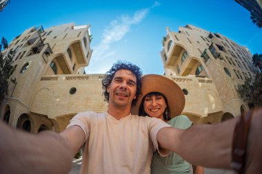 Yaz kıyafetleri içinde genç bir çift şehir caddesinde yürürken birbirlerine sarılıp selfie çekiyorlar. Sokakta selfie.