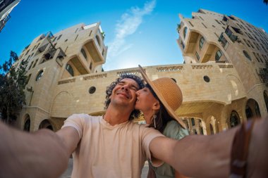 Yaz kıyafetleri içinde aşık genç bir çift şehir caddesinde yürürken öpüşüp selfie çekiyorlar. Sokakta öpücük.