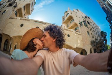 Yaz kıyafetleri içinde aşık genç bir çift şehir caddesinde yürürken öpüşüp selfie çekiyorlar. Sokakta öpücük.